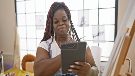 Téléchargez les photos : Femme artiste afro-américaine confiante et belle dessinant joyeusement sur pavé tactile, donnant vie à sa créativité dans un cadre de studio d'art moderne. - en image libre de droit