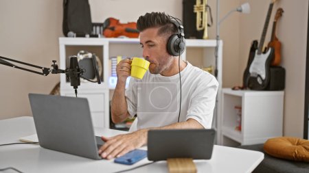 Foto de Atractivo joven hispano, un reportero profesional, hablando apasionadamente al aire en un acogedor estudio de radio, sosteniendo una taza de café - Imagen libre de derechos