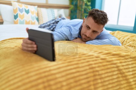 Téléchargez les photos : Jeune homme hispanique utilisant pavé tactile couché sur le lit dans la chambre - en image libre de droit