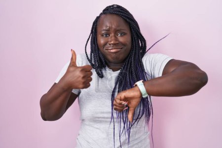 Photo for Young african woman standing over pink background doing thumbs up and down, disagreement and agreement expression. crazy conflict - Royalty Free Image