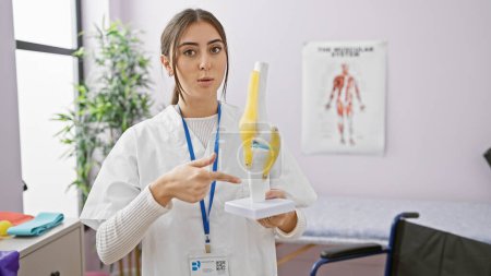 Téléchargez les photos : Une jeune physiothérapeute hispanique examine un modèle de genou à l'intérieur d'une clinique. - en image libre de droit