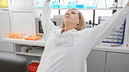Foto de Científica madura que se estira en un entorno de laboratorio, lo que indica un descanso o alivio del estrés. - Imagen libre de derechos