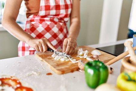 Photo for Young beautiful hispanic woman cutting onion at the kitchen - Royalty Free Image