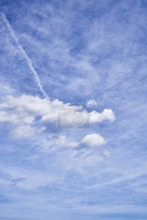 Téléchargez les photos : Un ciel serein avec des nuages épars et pelucheux, des traînées, un cirrus tortueux et une toile de fond bleu tranquille. - en image libre de droit