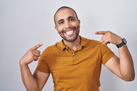 Téléchargez les photos : Homme hispanique avec la barbe debout sur fond blanc souriant gai montrant et pointant avec les doigts dents et la bouche. concept de santé dentaire. - en image libre de droit