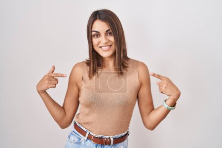 Foto de Young hispanic woman standing over white background looking confident with smile on face, pointing oneself with fingers proud and happy. - Imagen libre de derechos