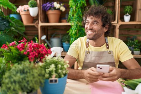 Photo for Young hispanic man florist smiling confident using smartphone at flower shop - Royalty Free Image