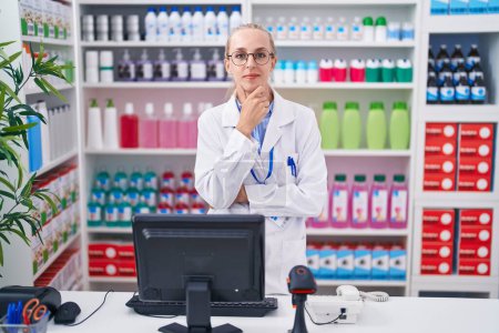 Photo for Young caucasian woman working at pharmacy drugstore looking confident at the camera smiling with crossed arms and hand raised on chin. thinking positive. - Royalty Free Image