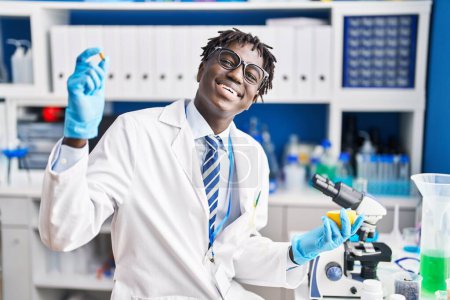 Foto de Hombre científico afroamericano sonriendo confiado sosteniendo píldora y limón en el laboratorio - Imagen libre de derechos