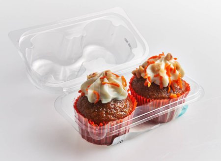 Téléchargez les photos : Deux cupcakes à la carotte avec glaçage au fromage à la crème dans un récipient en plastique sur fond blanc. - en image libre de droit
