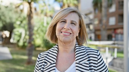 Photo for A smiling caucasian middle-aged woman in a striped jacket outdoors in a sunny park. - Royalty Free Image