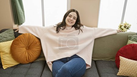 Foto de Mujer relajada descansando en el sofá con almohadas de colores en un acogedor entorno de sala de estar, que encarna la comodidad casera y el interior elegante - Imagen libre de derechos
