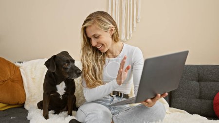 Téléchargez les photos : Une femme caucasienne profite d'un appel vidéo à la maison avec son chien et son ordinateur portable, mettant en valeur la compagnie et la technologie dans un cadre confortable. - en image libre de droit