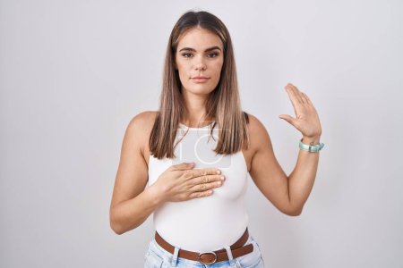 Photo for Hispanic young woman standing over white background swearing with hand on chest and open palm, making a loyalty promise oath - Royalty Free Image