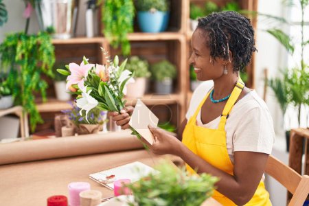 Téléchargez les photos : Middle age african american woman florist make selfie by smartphone holding lavender plant at flower shop - en image libre de droit