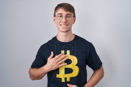 Photo for Caucasian blond man wearing bitcoin t shirt smiling and laughing hard out loud because funny crazy joke with hands on body. - Royalty Free Image