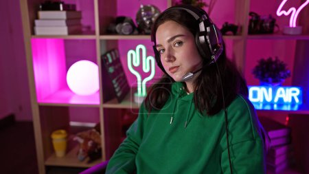 Photo for Portrait of a young woman wearing a headset in a vibrant gaming room at night, projecting a relaxed, tech-savvy image. - Royalty Free Image