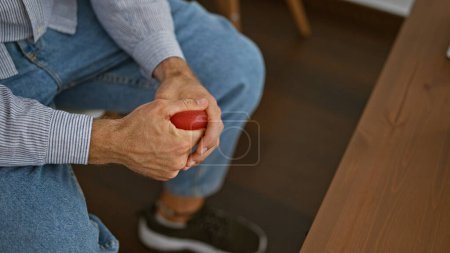 Téléchargez les photos : Jeune homme hispanique assis sur une chaise appuyant sur la balle avec la main dans la salle d'attente - en image libre de droit