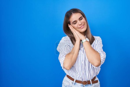 Photo for Hispanic young woman standing over blue background sleeping tired dreaming and posing with hands together while smiling with closed eyes. - Royalty Free Image