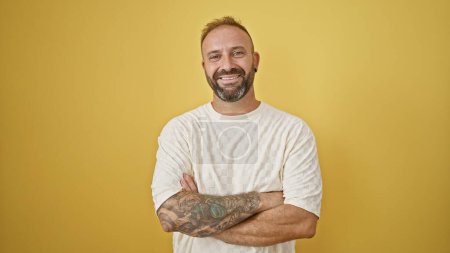 Photo for Attractive young man, standing with a confident smile and casual arms crossed gesture. isolated on a yellow background, exuding sheer happiness and positive joy. - Royalty Free Image