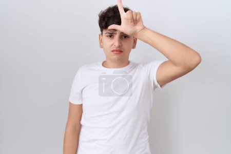 Photo for Young non binary man wearing casual white t shirt making fun of people with fingers on forehead doing loser gesture mocking and insulting. - Royalty Free Image