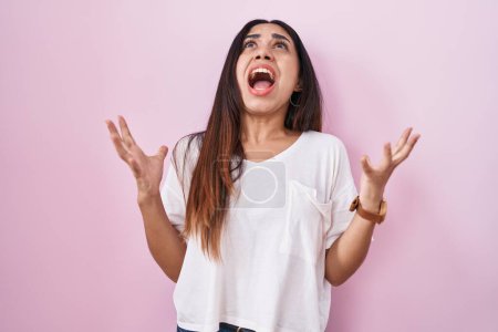 Photo for Young arab woman standing over pink background crazy and mad shouting and yelling with aggressive expression and arms raised. frustration concept. - Royalty Free Image