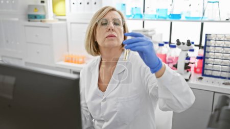 Téléchargez les photos : Femme scientifique mature examinant le tube à essai en laboratoire, portant des lunettes et un manteau de laboratoire à l'intérieur. - en image libre de droit