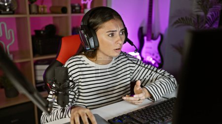 Photo for Hispanic woman reacts while gaming in a dark, colorful room with microphone and headset - Royalty Free Image
