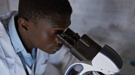 Photo for African man using microscope in laboratory setting, portraying science, healthcare, and education. - Royalty Free Image
