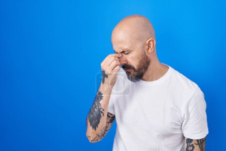 Photo for Hispanic man with tattoos standing over blue background tired rubbing nose and eyes feeling fatigue and headache. stress and frustration concept. - Royalty Free Image