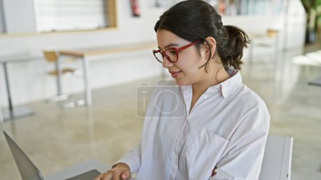 Photo for A young hispanic woman works attentively on a laptop in a bright modern office setting - Royalty Free Image