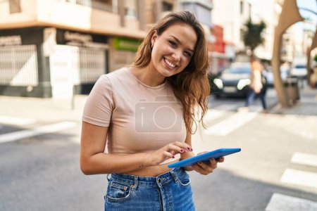 Téléchargez les photos : Jeune belle femme hispanique souriant confiant en utilisant touchpad à la rue - en image libre de droit