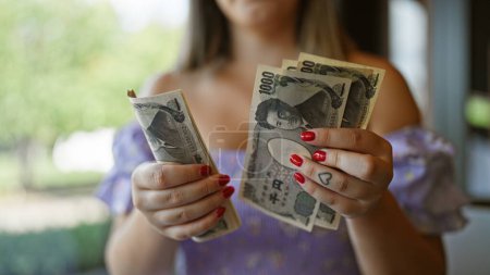 Photo for Savvy young caucasian woman counting her japan yen banknotes stash inside nostalgic cafeteria, engaging in smart finance decisions with her cash in hand, highlighting her wealth and rich savings - Royalty Free Image