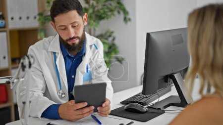 Photo for Young hispanic man doctor showing touchpad to patient at the clinic - Royalty Free Image