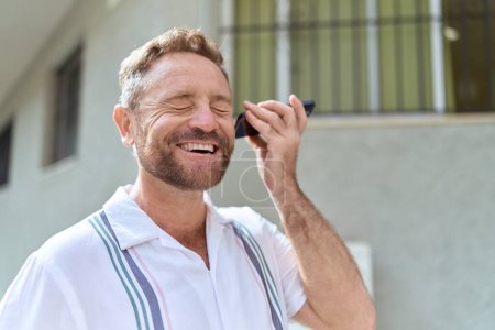 Foto de Middle age man smiling confident listening audio message by the smartphone at street - Imagen libre de derechos