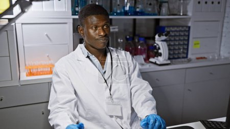 Photo for African man scientist in lab coat working in a laboratory with microscope and test tubes - Royalty Free Image