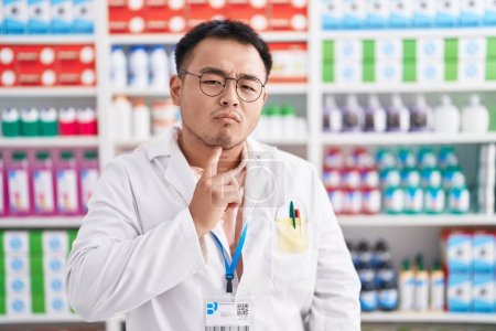 Photo for Chinese young man working at pharmacy drugstore thinking concentrated about doubt with finger on chin and looking up wondering - Royalty Free Image