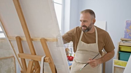 Photo for Handsome young man artist intensely drawing at his relaxed art studio, a creativity class bursting with paintbrushes, canvas and concentrated adult students. - Royalty Free Image