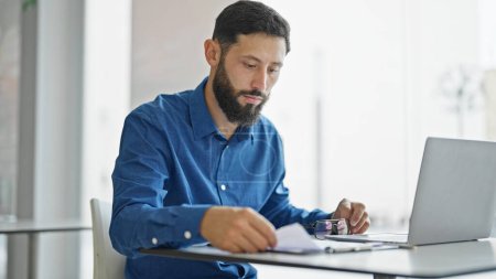 Téléchargez les photos : Jeune homme hispanique travailleur d'affaires en utilisant un document de lecture d'ordinateur portable au bureau - en image libre de droit