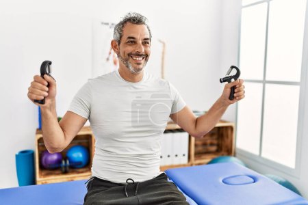 Photo for Middle age grey-haired man patient having rehab press machine with hands at rehab clinic - Royalty Free Image