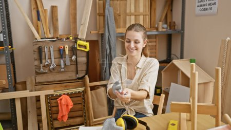 Foto de Joven sonriente disfrutando del trabajo de carpintería en un taller bien equipado lleno de herramientas de carpintería y madera. - Imagen libre de derechos