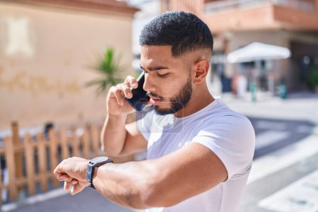 Photo for Young latin man talking on the smartphone looking watch at street - Royalty Free Image
