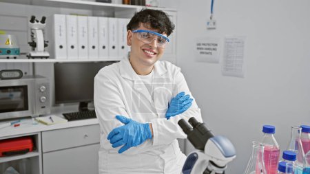 Foto de Hombre sonriente en labcoat con brazos cruzados se para en el laboratorio, retratando a un investigador científico profesional en el interior. - Imagen libre de derechos