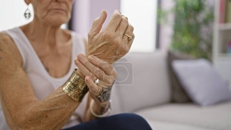 Photo for Elderly woman with short grey hair, suffering wrist pain, sitting on sofa at home - Royalty Free Image