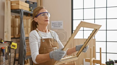 Photo for A mature woman examines furniture in a carpentry workshop, surrounded by tools. - Royalty Free Image