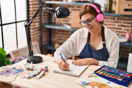 Photo for Middle age woman artist listening to music drawing at art studio - Royalty Free Image