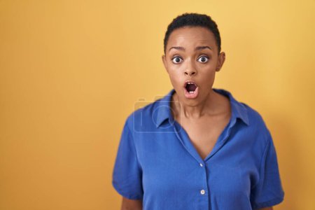 Photo for African american woman standing over yellow background afraid and shocked with surprise and amazed expression, fear and excited face. - Royalty Free Image