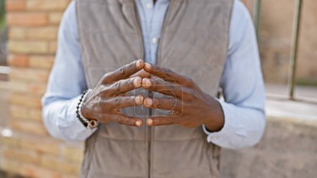 Photo for Close-up of an unidentifiable african man's folded hands with a stylish bracelet, standing in an urban setting. - Royalty Free Image
