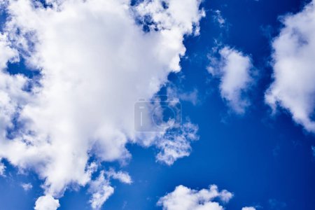 Photo for Fluffy white clouds scattered across a vibrant blue sky convey a sense of tranquility and open space. - Royalty Free Image