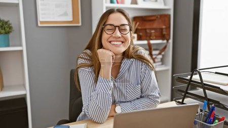 Photo for Smiling woman with glasses seated in a modern office, showcasing professionalism and cheerful demeanor. - Royalty Free Image